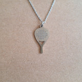 A stainless steel padel racket pendant with a chain, displayed against a cardboard background.