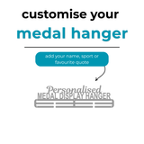 A personalized metal medal display hanger. Large text above reads 'Personalised MEDAL DISPLAY HANGER' with smaller text 'customise your medal hanger' and 'add your name, sport or favourite quote'.