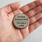 Hand holding a circular metal badge with motivational quote on a light background