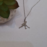 A silver-toned chain necklace with a small pendant of a woman playing hockey, displayed on a light surface next to a green succulent plant