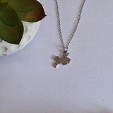 A silver-toned chain necklace with a small silhouette pendant of a rider on a horse displayed on a light surface next to a white planter with green leaves.