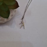 A silver-toned necklace with a minimalist silhouette pendant of a netball player, displayed on a light off-white surface next to a green succulent in a textured pot.