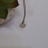 A stainless steel metal necklace with a small paw print pendant, displayed on a light off-white surface next to a green succulent in a white pot