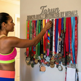 Woman in athletic wear reaching for medals on a wall display with 'Taryn Ridiculously Motivated by Medals' text.