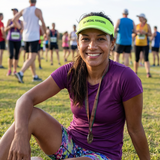 A woman sitting on grass after a run, wearing a yellow peak visor with SA Medal Hangers text.