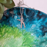 A silver-toned metal pendant necklace featuring a silhouette of a person playing cricket displayed on a textured, iridescent blue and green ceramic plate.