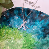 A silver-tone chain necklace with a silhouette pendant of a person playing Hockey, displayed on a glossy, iridescent green and blue ceramic plate.