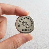 Hand holding a button with 'one more step, repeat' text on a light background