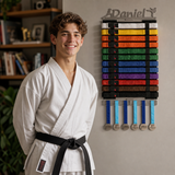 Person in a white martial arts uniform standing next to a wall display of colored belts and medals.