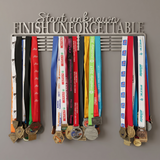 A large Stainless steel Medal holder with various medals hanging on a gray background with the quote Start Unknown Finish Unforgettable by SA Medal Hangers
