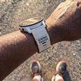 A person wearing a smartwatch with a 'STRONG ENOUGH'watch tag on a road. SA Medal Hangers