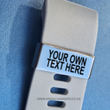 Personalizable metal tag on a white strap with blue accents against a blue background