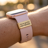 Smartwatch with a motivational band on a wrist against a blurred natural background with the text You've got this KEEP MOVING on the watch tag