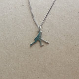 A silver-colored stainless steel pendant in the shape of a female hockey player on a chain, displayed against a brown background.
